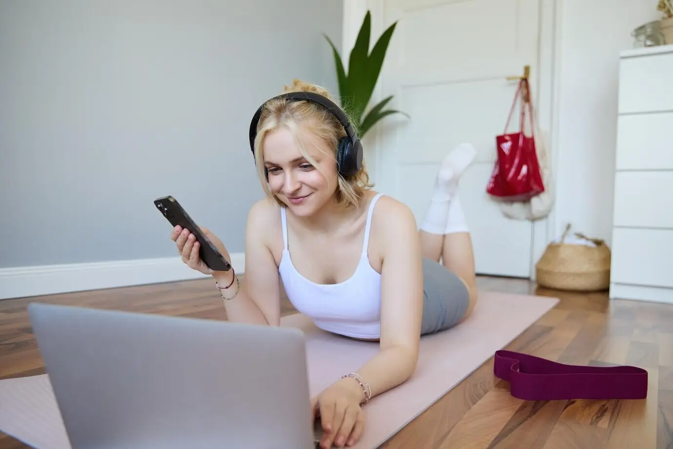 Portrait of a young woman wearing headphones, lying on a rubber mat, and watching exercise videos on a laptop while working out.