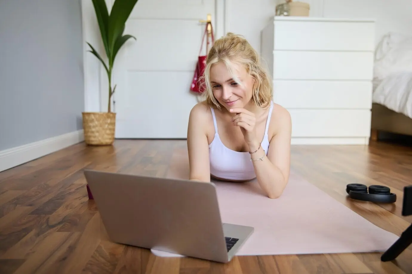 Portrait of a beautiful blond woman watching fitness video tutorials on a laptop while lying on rubber yoga